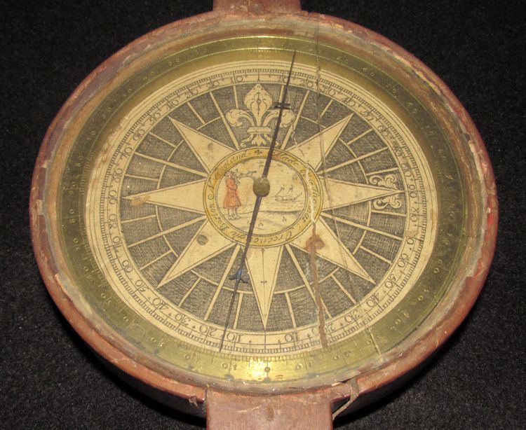 Thomas Greenough (1710–1785). Surveyor's compass or circumferentor, ca. 1760 [Historic Maps Collection]. Diameter (including frame), 6.25 inches; between the sights, 12 inches; height, 6 inches. Cherrywood stand and frame support. The paper compass card shows a man in a red coat looking out to sea with a quadrant instrument, and a sailing vessel rides on the horizon. The card has eight points, like a star (one is a fleur-de-lis), and bears printed divisions of 0° to 90° in each of its four quadrants. The inscription reads, "Made by Thomas Greenough, Boston, New England." Greenough was an American colonial instrument maker.
